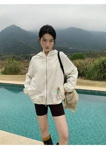 Aziatisch model in een witte outdoor jas met capuchon en zwarte wielrenbroek bij het zwembad
