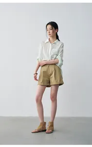 Full view of woman wearing khaki cuffed shorts with pleated details in minimalist setting.