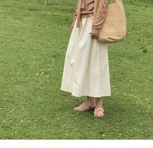 Gros plan d'une jupe-culotte crème sur l'herbe, assortie d'un sac et sandales