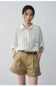 Close-up of women's khaki pleated shorts with cuffed hem and brown leather belt.