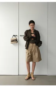 Mujer con pantalones cortos caqui con dobladillo y camisa marrón en estudio minimalista