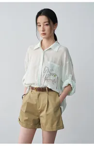Detail view of women's khaki pleated shorts with rolled-up cuffs and a brown leather belt
