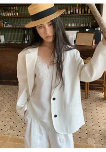 Dettaglio di un blazer bianco minimalista stile commuter con top in pizzo in un bar.