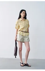 Woman wearing pleated khaki summer shorts with yellow striped shirt and brown accessories.