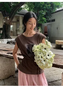 Femme en t-shirt marron à manches courtes et imprimé, tenant des fleurs blanches.
