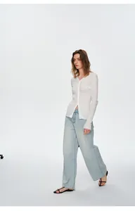 Vrouw draagt een witte gebreide cardigan met V-hals en een lichtblauwe wijde jeans