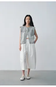 Scatto di moda a figura intera di modella in gilet di jeans grigio e pantaloni bianchi larghi