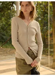 Model draagt een beige ribgebreid vest met V-hals in een natuurlijke buitenomgeving