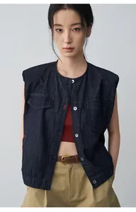 Dettaglio di un gilet in denim blu scuro a girocollo sovrapposto a un top rosso.