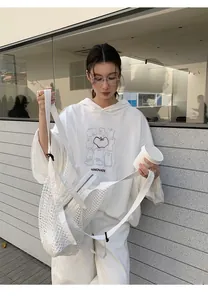 Young woman in white hooded sweatshirt with graphic print holding a mesh bag.