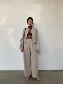 Full body shot of model wearing oatmeal cropped zip-up sweatshirt and wide-leg trousers.