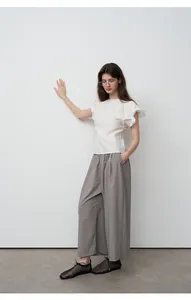Model draagt een ontspannen grijze broek met wijde pijpen en een witte top met ruches.