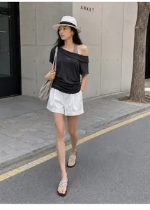 Model wearing a black off-shoulder layered t-shirt with white shorts in urban street setting
