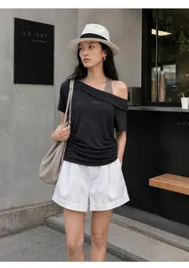 Model wearing an off-shoulder two-piece ruched T-shirt and white shorts in urban cafe.