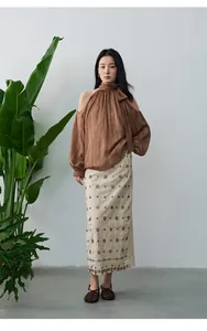 Ganzkörperansicht einer Frau in brauner Neckholder-Bluse und besticktem Rock im Urlaubsstil