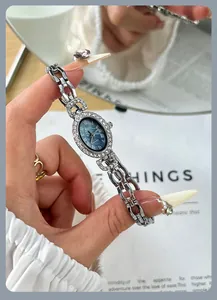 Nahaufnahme einer ovalen Quarzuhr im Vintage-Stil mit Strasssteinen und Silberarmband