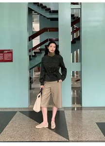 Fashion model wearing high-waist tan PU leather culottes in a modern architectural scene.