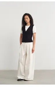 Modell trägt schwarze Strickweste mit Polokragen und weiße Hose mit weitem Bein im Studio