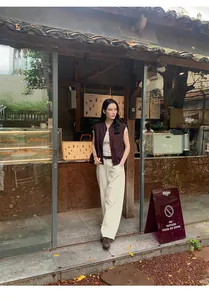 Dettaglio di un gilet scamosciato marrone abbinato a pantaloni bianchi in un caffè.
