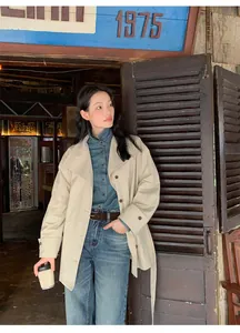 Vue détaillée d'un trench-coat beige minimaliste porté par un mannequin en extérieur.