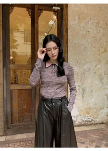 Stylish woman in pink knit polo and black wide-leg PU leather pants against a rustic wall.