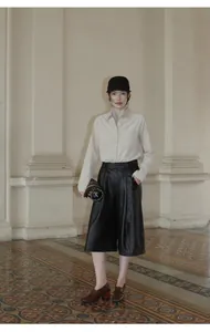 Model wearing autumn high waist black PU leather wide-leg culottes in a classic hall setting