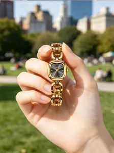 Close-up of gold chain watch with square black dial held in hand