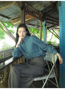 Young Asian woman in a denim shirt and grey wide-leg pants posing in a rustic wooden cabin
