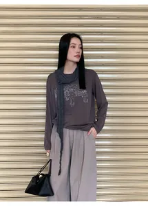 Modelo asiática con camiseta de algodón Tencel marrón holgada y detalle de bufanda gris.