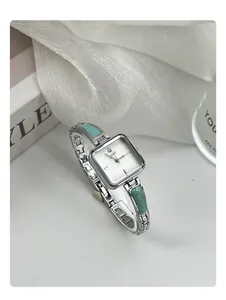 Close-up of silver women's quartz watch with square white dial and green stone inlay detail
