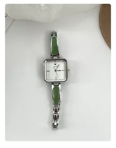 Macro view of women's elegant square quartz watch with silver strap and green inlays