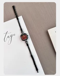 Elegant detail of a vintage square lady's quartz watch with a red dial and black mesh strap