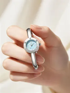 Detailed view of an elegant silver-toned bangle watch with a light blue dial held by a hand.