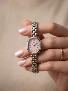 Close-up of a vintage JW oval quartz watch with a pink dial and silver chain strap.