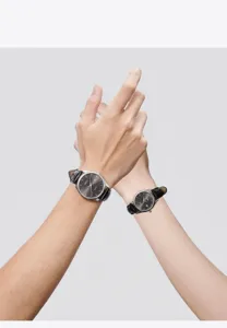 Detail view of GEDI couple watches with black leather straps and sunburst dials on wrists