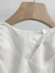 Dettaglio della chiusura posteriore con bottone e scollatura a goccia su abito bianco