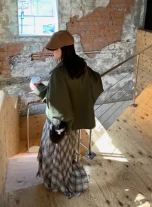 Detail of a brown plaid irregular midi skirt styled with a green jacket on wooden stairs.