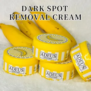 Close-up detail of Adeus dark spot removal cream jars presented with yellow banana props