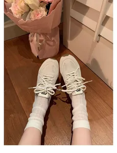 Detailansicht der beigen Ballett-Core Sneaker mit Perlenschnürsenkeln auf Holzboden