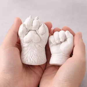 Close-up of white 3D plaster casts showing a pet paw and a baby fist held in hands