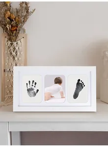 White memorial frame featuring baby's handprint, footprint and a photo on desk