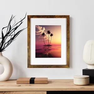 Cadre photo artisanal en bois marron avec imprimé palmier au coucher du soleil sur un mur blanc.