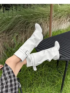 Detailweergave van witte slouchy laarzen met gespen gedragen in een buitenomgeving