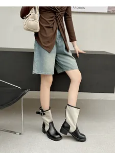 Model wearing retro two-tone patchwork western cowboy boots in a lifestyle setting.