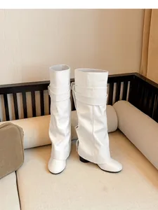 Detailansicht weißer Hosenstiefel mit lockerem Lederdesign auf einem beigen Sofa