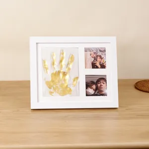 White DIY memorial photo frame with golden handprint clay mold and couple photos.