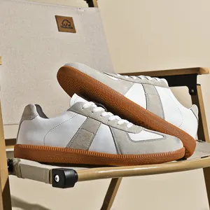 Sneaker bianche retro GAT con camoscio grigio e suola in gomma su una sedia.