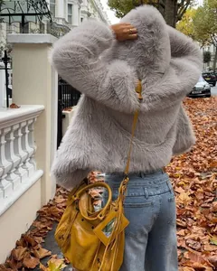 Back view of a grey faux fur hooded jacket styled with a yellow bag on an autumn street