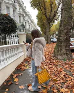 A stylish grey hooded faux fur jacket for women shown in a cozy autumn street setting.