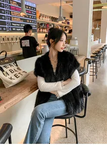 Dettaglio di un gilet nero in ecopelliccia con scollo a V in un ambiente da caffè accogliente